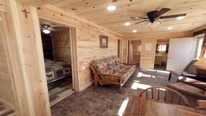A wooden cabin interior with a bed, sofa, dining table, and ceiling fan.