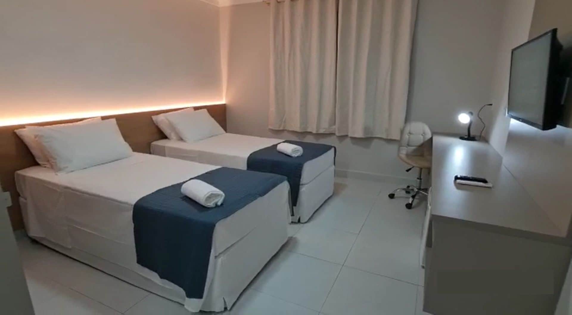 A hotel room with two beds, a desk with a computer, and a TV.