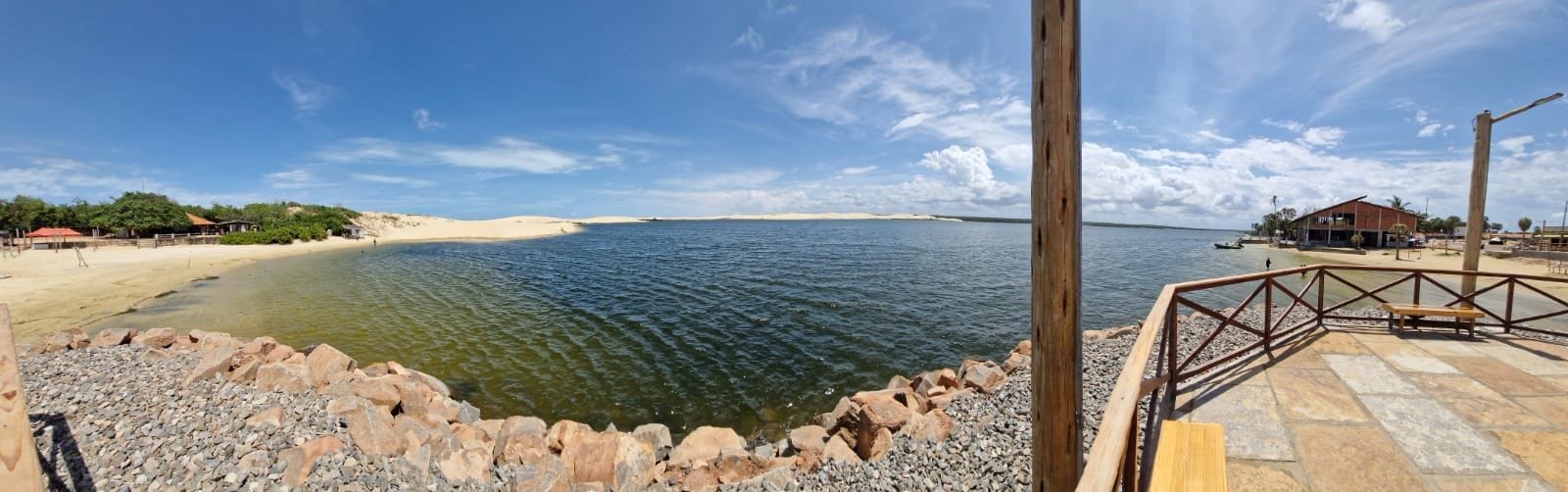 Een strand met een houten looppad dat naar een gebouw met een rood dak leidt.