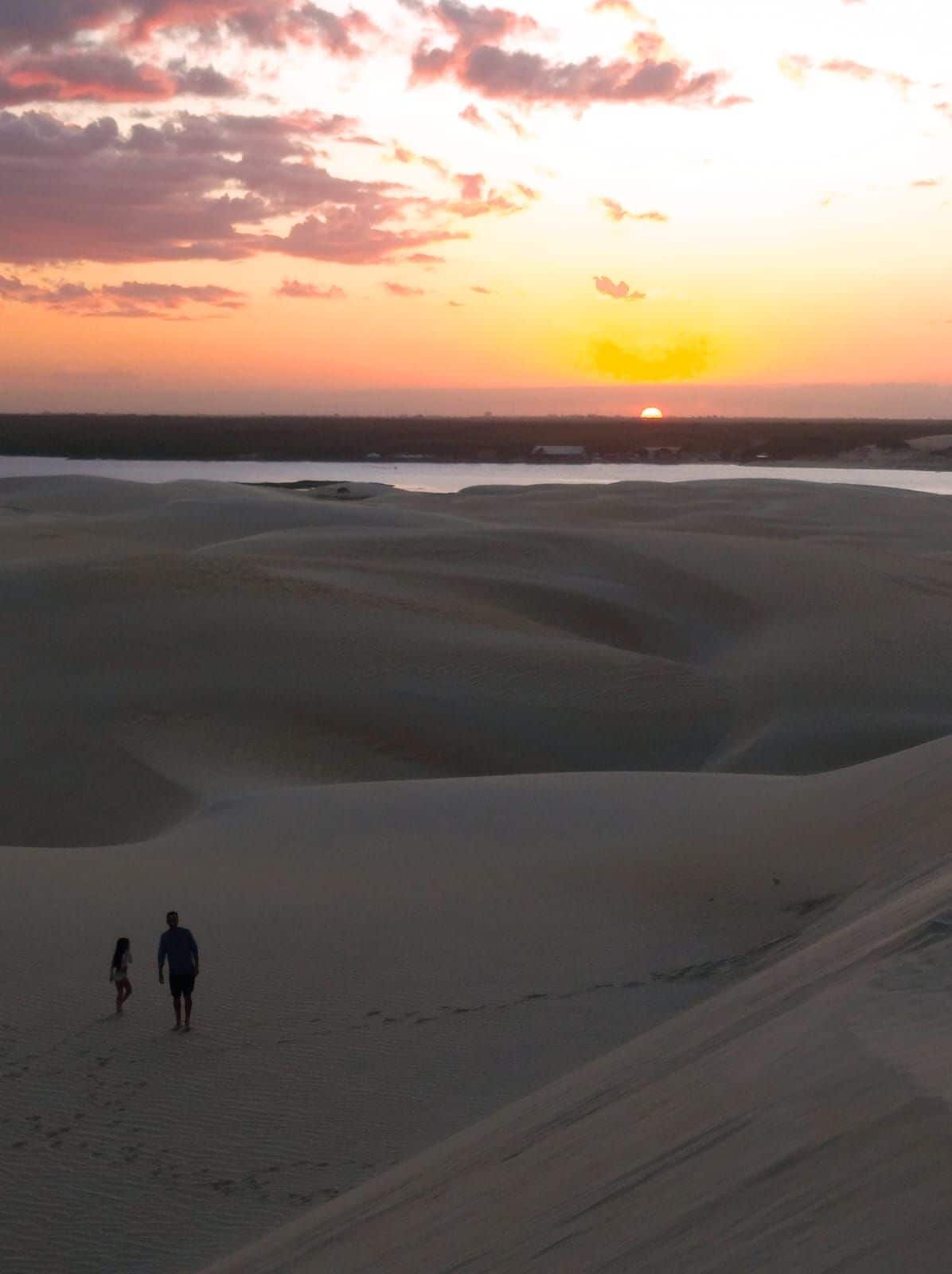 Paisaje desértico con dunas de arena y una puesta de sol al fondo.