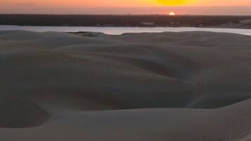 Paisaje desértico con dunas de arena y una puesta de sol al fondo.
