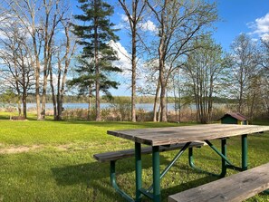A picnic table with benches in a grassy area with trees and a body of water in the background.