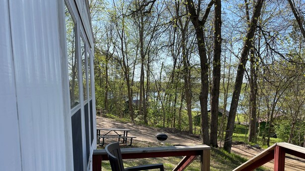 Eine Holzterrasse mit Picknicktisch und -stühlen, mit Blick auf ein bewaldetes Gebiet und einen Feldweg, der zu einer Hütte führt.