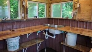 Ein rustikales Blockhaus mit Holzwänden, einer Holztheke, einem Waschbecken und zwei Fenstern.