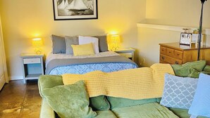Une pièce confortable avec un lit, un canapé vert, une petite table et une lampe.