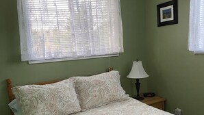 A bedroom with a bed, a nightstand, a lamp, a teddy bear, and a framed picture on the wall. - Hilltop Cottage (Cape Broyle)