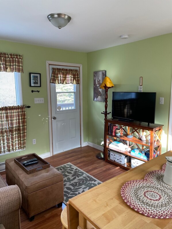 A living room with a television on a wooden stand, a small table, a sofa, and a door with curtains.