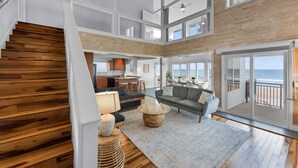 A spacious living area with a wooden staircase, a kitchen, and a balcony with a view of the ocean. - Pool, 7 Bed 7 Bath, Direct Oceanfront, 4 Kitchens (Port Orange)