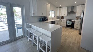 Een moderne keuken met witte kasten, een centraal eiland met barkrukken, een inbouwoven en een groot raam met uitzicht op een zwembad.