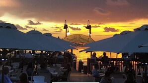 Een terras met parasols en tafels, met uitzicht op een waterpartij bij zonsondergang.