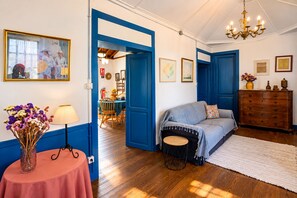 Ein Zimmer mit blauer Tür, einem Sofa, einer Holzkommode und einem Essbereich im Hintergrund.