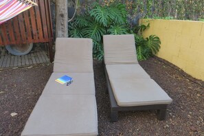 Two sun loungers with cushions, a small blue book, and a striped umbrella.