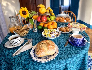 A breakfast table with various food items, a glass of orange juice, a cup of coffee, and a vase with a sunflower.