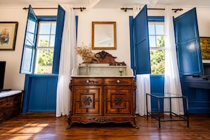 Une pièce avec un meuble en bois, un miroir et des volets bleus aux fenêtres.
