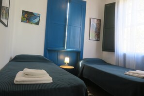 A hotel room with two beds, a nightstand with a lamp, and artwork on the walls.