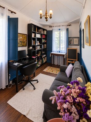 Ein Zimmer mit Schreibtisch, Stuhl, Bücherregal, Sofa und einem kleinen Tisch mit Lampe.