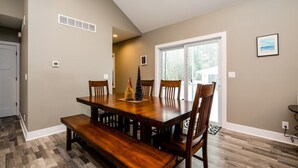 Comedor con mesa y sillas de madera, un banco, un pequeño árbol de Navidad y una puerta que da a otra habitación.