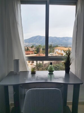 Une pièce avec une grande fenêtre, un bureau et deux plantes en pot.