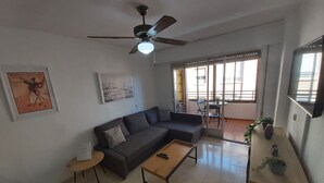 Un soggiorno con divano, tavolino, ventilatore a soffitto e un balcone con tavolo e sedie.