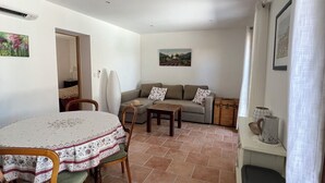 A spacious living area with a dining table, chairs, a sofa, and a trash bin. - Modern apartment 10min to walk to the city center WITH swimming pool (Cotignac)