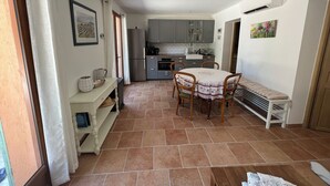 A compact kitchen with grey cabinets, a built-in oven, and a refrigerator. There is a dining area with a round table and chairs, and a bench along the wall. - Modern apartment 10min to walk to the city center WITH swimming pool (Cotignac)
