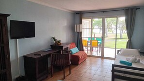 Habitación de hotel con cama, escritorio, televisión, sofá y balcón con sillas.