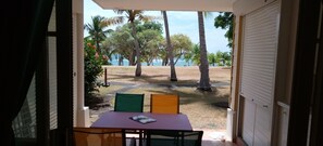 Vista desde una habitación con una mesa y sillas, con vistas a un área verde con palmeras y un cuerpo de agua.