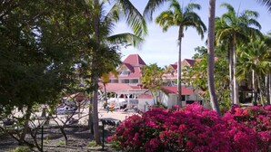 A resort with a red-roofed building surrounded by palm trees and pink bougainvillea. - Studio 4 pers vue mer et cocotiers Village Vacances Ste-Anne, Pointe du Helleux (Sainte Anne)