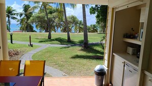 A patio area with a view of palm trees and the ocean. There is a table with chairs and a trash can. - Studio 4 pers vue mer et cocotiers Village Vacances Ste-Anne, Pointe du Helleux (Sainte Anne)