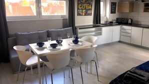 A modern kitchen with white cabinets, a dining area with a white table and chairs, and a grey sofa. - KW38 - 2 min to Old Market Square and Townhall (Wroclaw)