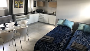 A modern hotel room with a kitchenette, a dining area with a white table and chairs, and a bed with blue bedding. - KW38 - 2 min to Old Market Square and Townhall (Wroclaw)