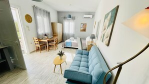 A modern living room with a blue sofa, a dining table with chairs, a small coffee table, and a bed with a blue headboard. - Villa Arietta Santorini (Santorini)
