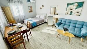 A modern, well-lit room with a bed, a sofa, a dining table set for two, and a desk. - Villa Arietta Santorini (Santorini)