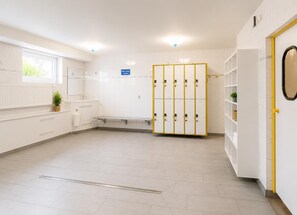 Een schone, goed verlichte kleedkamer met witte kasten, een bank en een kleine plant.