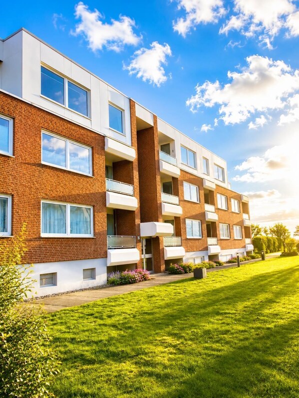 A multi-story residential building with a brick facade, balconies, and a well-maintained lawn.
