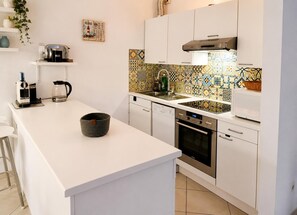 Een moderne keuken met witte kastjes, een centraal eiland, een koffieapparaat en een decoratieve spatwand.