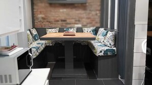 Una cucina compatta con zona pranzo, caratterizzata da una parete in mattoni, elettrodomestici moderni e una piccola finestra.