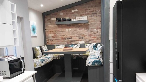 Una cucina moderna con forno a microonde integrato, una zona pranzo con una panca e una parete in mattoni con un cartello 'Home'.