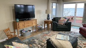 A living room with a television, a sofa, a chair, a coffee table, and a view of the outdoors. - Spacious Lakefront Home with Amazing View (Huron)