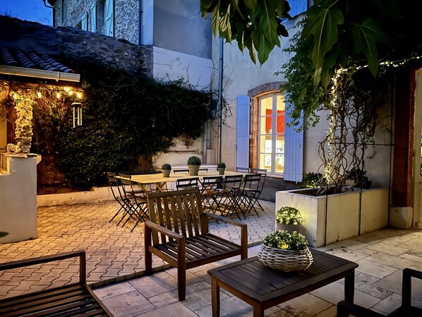 An outdoor patio area with a table and chairs, surrounded by potted plants and a stone wall.