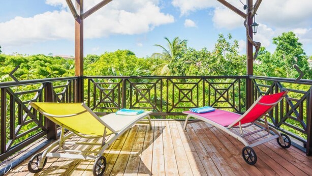 Une terrasse en bois avec deux chaises longues et une petite table, offrant une vue sur un paysage verdoyant et luxuriant.
