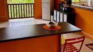 Une cuisine compacte dotée d’un îlot central, d’un réfrigérateur et d’une fenêtre donnant sur un espace verdoyant.