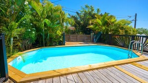 Une piscine rectangulaire dotée d’une terrasse en bois et d’un escalier en métal, entourée d’une végétation tropicale luxuriante.
