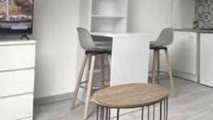 Et moderne køkken med hvide skabe, en mikrobølgeovn og et spiseområde med et rundt bord og to barstole.