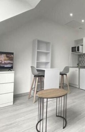 Una cocina moderna con armarios blancos, microondas y un comedor con una mesa redonda y dos taburetes de bar.