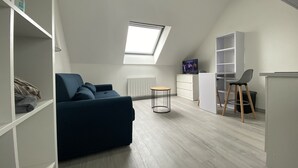En moderne, lys stue med en blå sofa, et rundt bord, et fjernsyn og et ovenlysvindue.