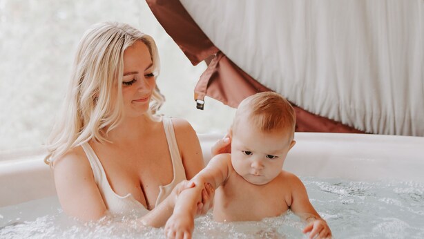 Eine Frau und ein Baby in einer Whirlpool-Badewanne mit Blick auf Bäume.
