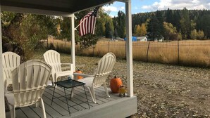 Eine überdachte Terrasse mit Adirondack-Stühlen, einem kleinen Tisch und einer amerikanischen Flagge.
