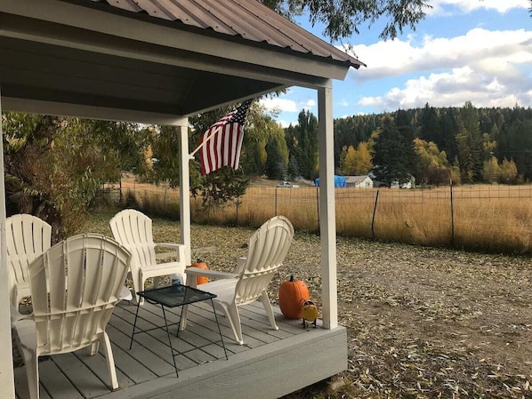 Un patio techado con sillas Adirondack, una mesa pequeña y una bandera estadounidense.