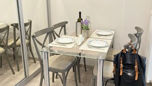 En matplats med ett glasbord, grå stolar, en svart ryggsäck och en tavla på väggen.